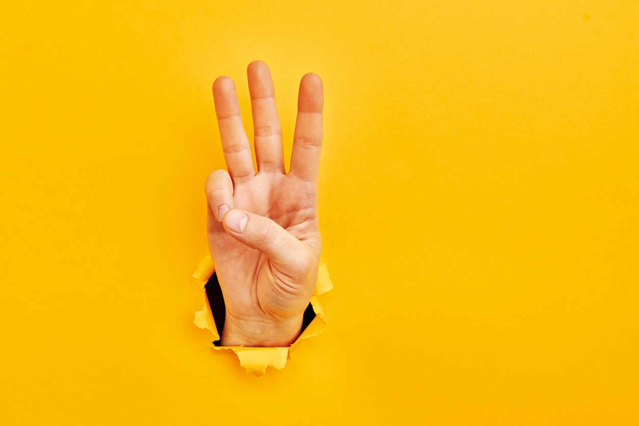 Human hand reaching through torn yellow paper sheet showing number three