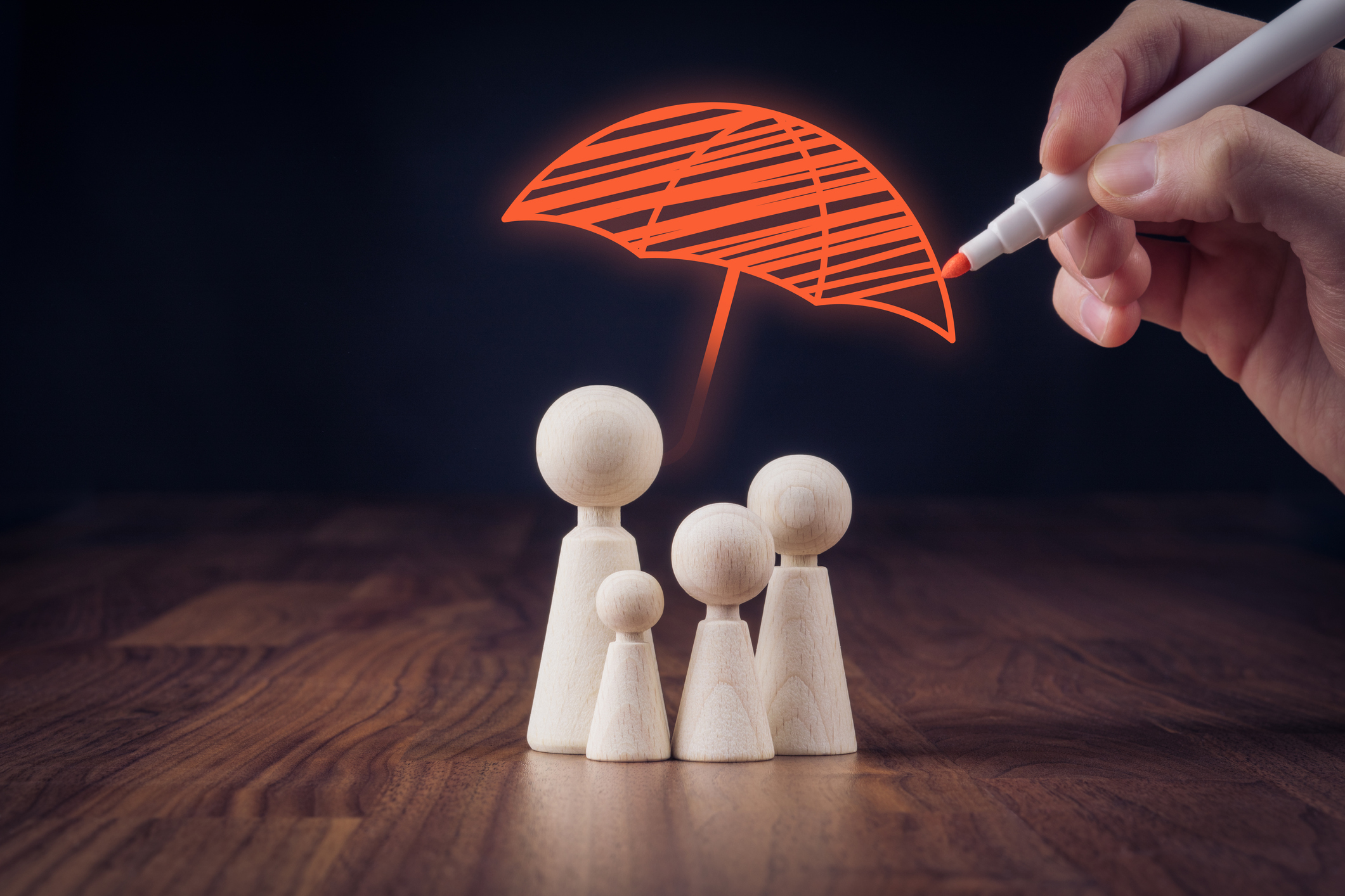 Family life and property insurance concept. Wooden figurines representing family and hand drawing umbrella, symbol of insurance.