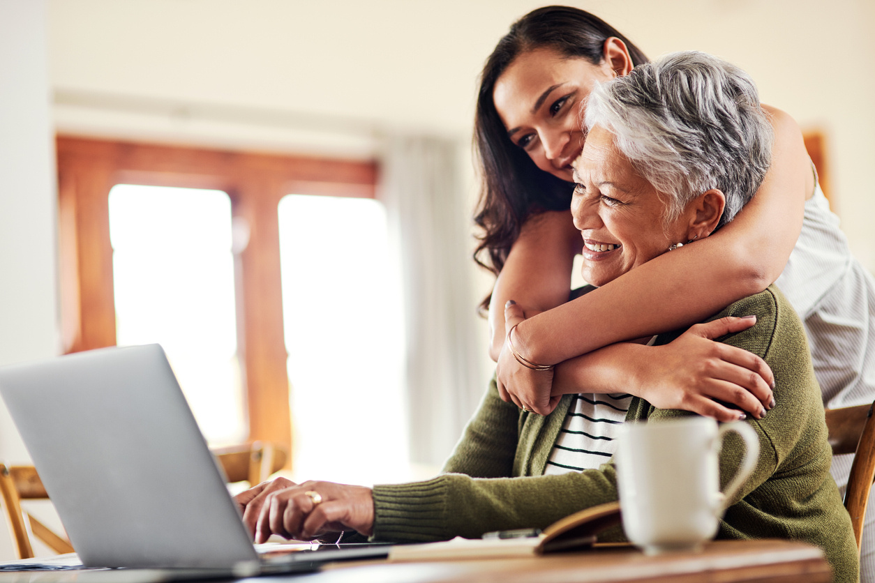 Cropped shot of young woman hugging her grandmother & helping her with her finances on a laptop