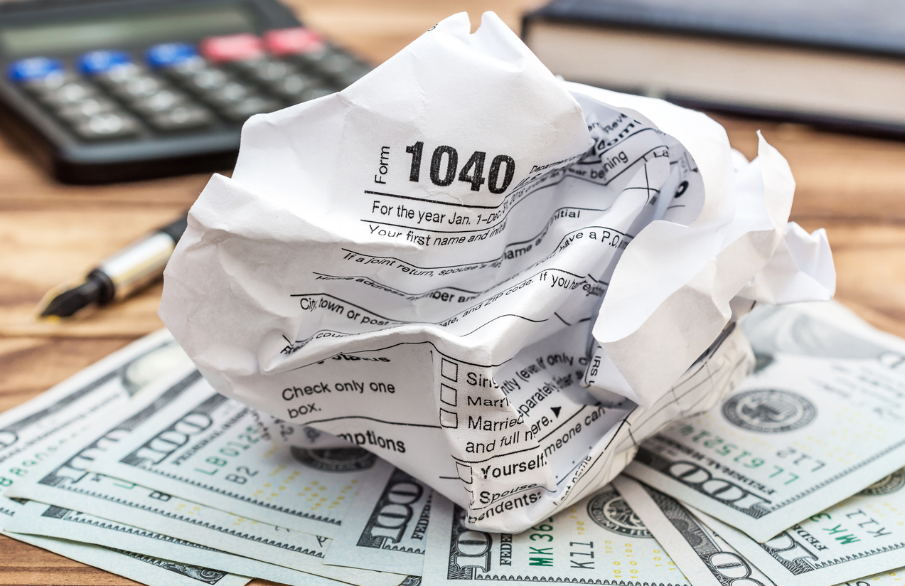 Crumpled tax form with money, calculator and notepad on the table.