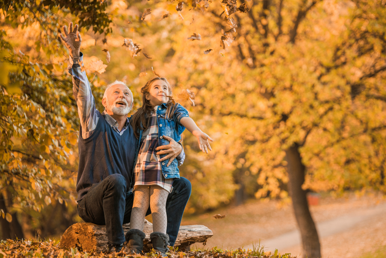 Photo of a grandfather and his granddaughter loving autumn. Throwing leaves in the air.